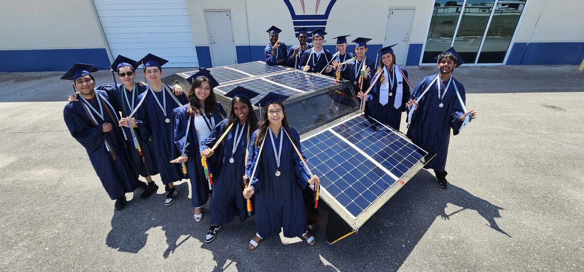 Team members in graduation caps and gowns gathered around the solar car,
                      whose upper surface is covered in solar panels.